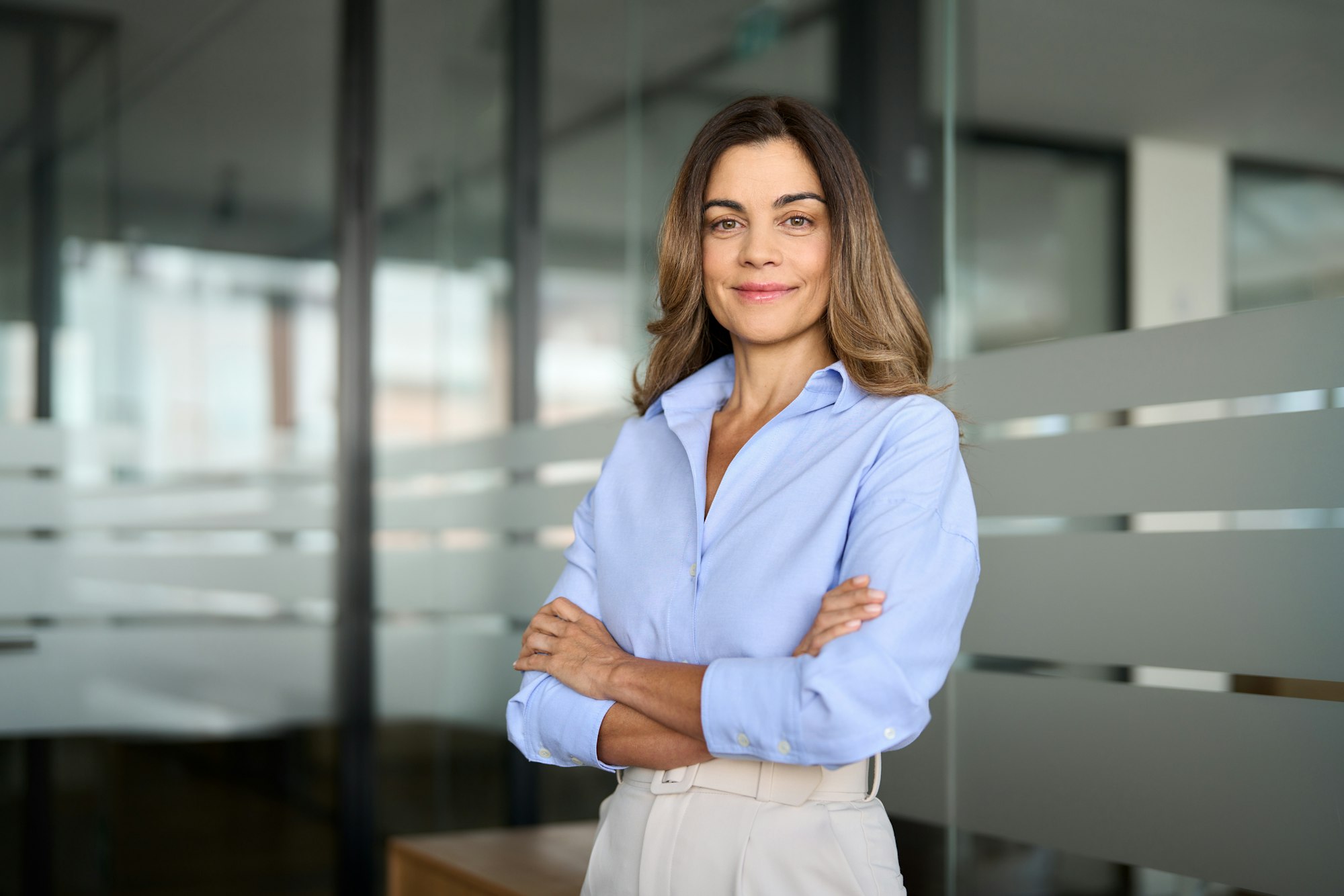 Middle aged business woman standing in office arms crossed. Portrait.